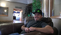 Thumbnail of Tanner Flake sitting in a large arm chair at a hotel hosting the East Idaho Fly Tiers Expo in Idaho Falls, ID, people walk by in the background.