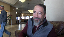 Thumbnail of Joe Pehrson sitting in a large arm chair at a hotel hosting the East Idaho Fly Tiers Expo in Idaho Falls, ID, people walk by in the background.