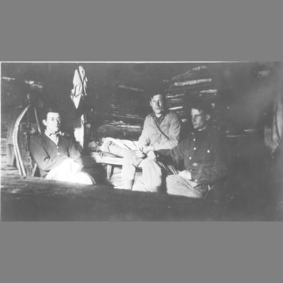 Three Men Seated Within a Very Dark Log Cabin Resting from Skiing