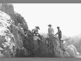 Men and Women Climbing a Rock Formation with Mountain Valley Visible in Distance
