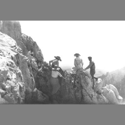 Men and Women Climbing a Rock Formation with Mountain Valley Visible in Distance