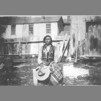 Bannock Chief Seated with Blanket and Broad Brimmed Hat by Wood Plank Building