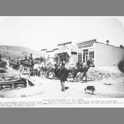 Wagons pulled up in front of wooden frame storefronts in Rochester, Montana, circa 1900s.