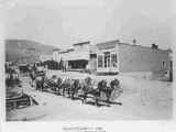 Freight team of eight horses passing by wood frame storefronts, circa 1900s.