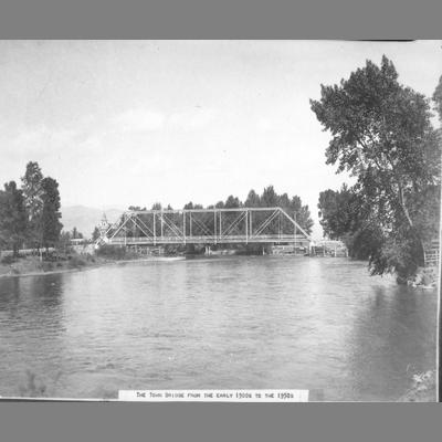 Metal truss bridge with trees along the bank in the early 20th century.