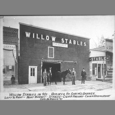 Three men and a horse pose in front of Willow Stable next to the Meat Market, circa 1890.