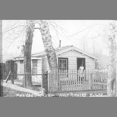 Mrs. George Pitcher Stands in Doorway of White Frame Home