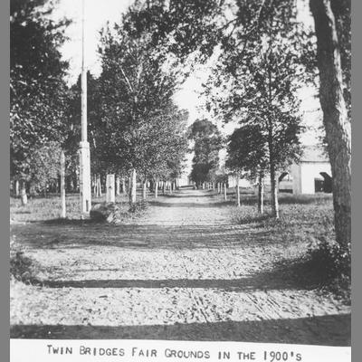 A head on view of a tree-lined dirt road into Twin Bridge's fairgrounds, circa 1900.