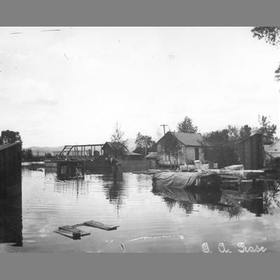 Flood of standing water, surrounded buildings, and piles of tarp covered lumber.