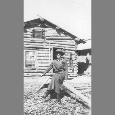 Unidentified Woman Sitting on Rail Fence in Front of Abandoned Log Cabin, circa 1920s