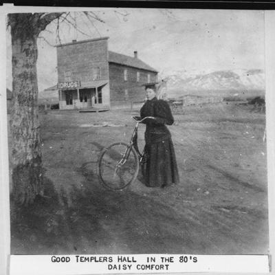 Woman in Academic Regalia poses next to a bicycle near Good Templers Hall, Twin Bridges, Montana.