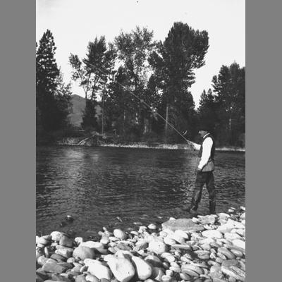 Unidentified man fishing on the edge of a river.