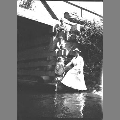 Woman stands next to three children near water.