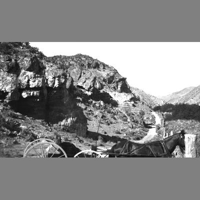 Cart-drawn by a horse next to a trail, next to a rock cliff.