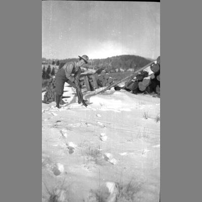 A man shovels snow next to a wood pile.