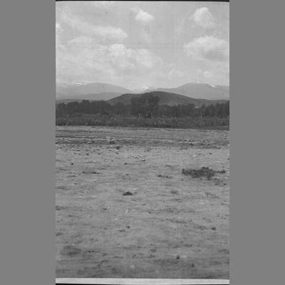 Image of a rocky field with hills and mountains in the background. A cowboy can be seen in the distance near the fence line.