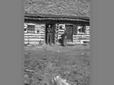 Two Unidentified Men Standing Outside A Log Home