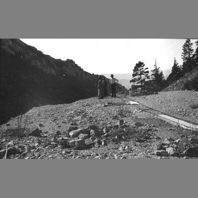 A Man and Two Women Stand Looking Off a Cliff With Railroad Tracks Next to Them