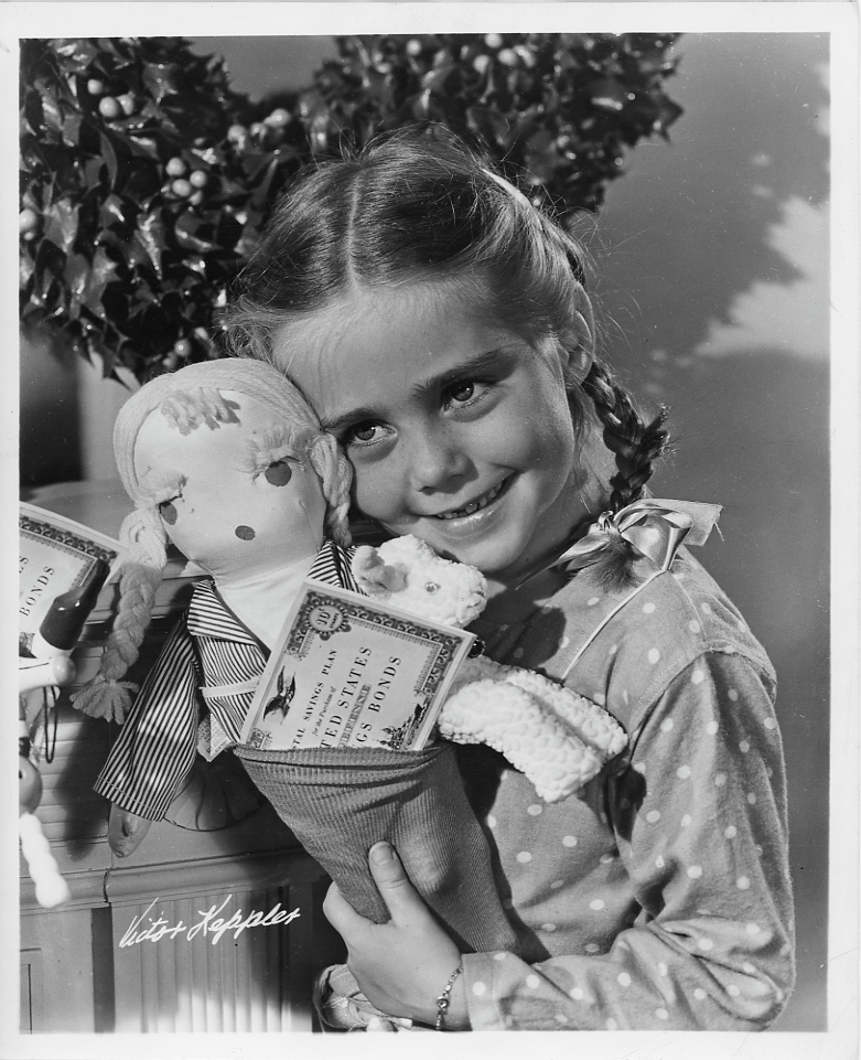 Girl in promotional picture smiling with a doll and war bonds