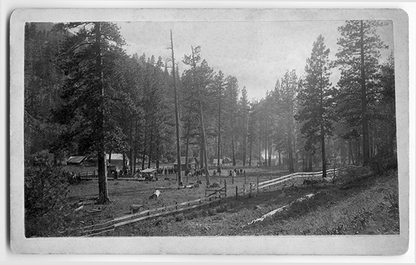 A few Buildings Nestled Among the Trees, People Standing in the Field, Unknown Location