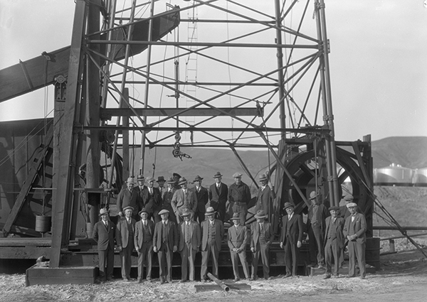 Group Portrait Standing in Front of Oil Drilling Rig, Unknown Location