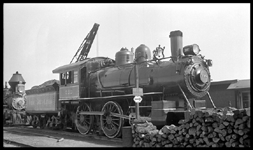 NYC 999  Chicago  9/34 New York Central 4-4-0 in new paint with elaborate striping for exposition  Boom of crane [for coal loading?] in bkgrnd and stack of cordwood in foreground indicate this may be the servicing area for the locomotives on display.  One older, smaller loco with diamond stack on track behind 999, cropped