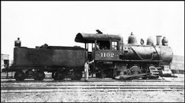NP 1102, Class L-9 locomotive with crew member on the ground posing for camera.