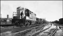 NP 551, EMD GP-7 road switcher with switchman poses on front platform while connected to a freight drag in Duluth switch yards.