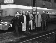 The blue flag is on the engine, so nothing will be moving for a while as a crowd of family and friends and railroaders join to have their picture taken with Mr. Yost, locomotive engineer, ending his career this 1962 winter day, with a last run on the Mainstreeter.