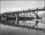 NP XE crossing bridge west of Thompson Falls, and making a mirror image in the water of the train crossing the bridge. 