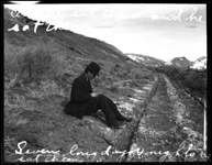 William Nixon sitting by the edge of a wagon ruts (trail). Caption on Photo says 