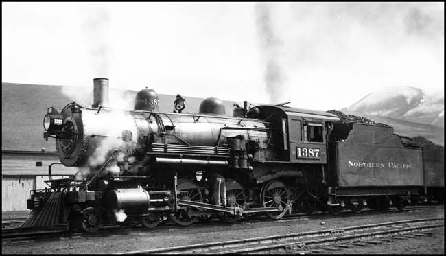 NP 1387, Class S-4 outside Roundhouse at Missoula. Mechanic working on running gear under boiler.