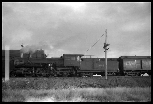 CB&Q 2004, 2-6-2 attached to baggage car pulling passenger train out of Frannie, WY.  Cab windows blocking view of cab and crew.