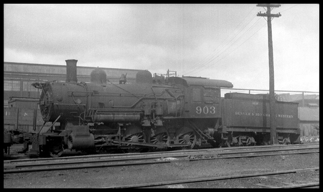 A bigger 2-8-0, a product of Baldwin Locomotive Works in 1900, waits out a depression with other derelict rolling stock.  This engine will probably never run again