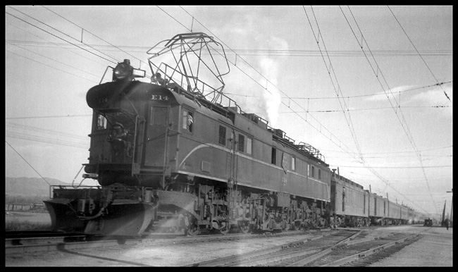 The pattern of wires on an electric railroad at even a minor division point could form an impressive web.  The Olympian, with a burst of steam from its train heating boiler is ready to go west on a cold autumn day