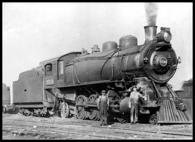 NP 1530  Missoula  cy Jeffery RF 3/4 view of class W 2-8-2, and engineer/fireman on ground  Engine has old style electric headlight, no tender lettering, the original arched cab window and locomotive number on cab side covered by framed glass  Crew is unidentified