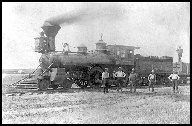 B&M 120  dup #4686 [4686 reads B&M 120 between Billings and Pacific Junction 1884 when building CB&Q into Billings  cy Ruffel from Levan] Left side view of 4-4-0 wood burner  Five crew members standing in front of locomotive, and a sixth is standing on a loaded gondola behind the tender  Copy negative