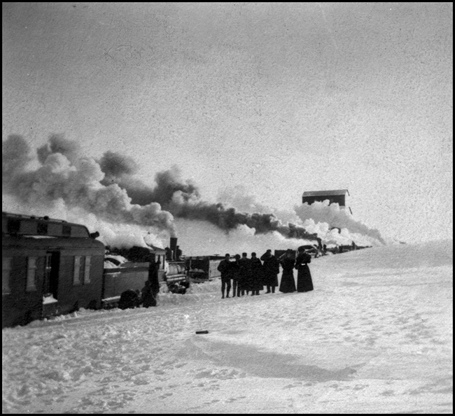 NP trains stalled in snow storm on Dak Divn about 1913  cy  D S Colby  Some of the men standing in the snow appear to be wearing trainmen's hats  The women may be passengers  There appears to be a coal dock in the background  The old Dakota Division stretched from Fargo to Mandan, and included several branch lines