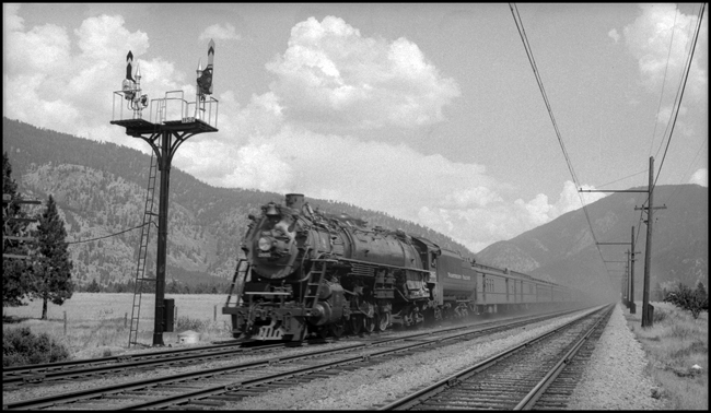 NP train No. 1 with NP 2665, Class A-3 and passenger cars near Missoula, MT and adjacent to Milwaukee track so that Milwaukee catinary is visible.  Also NP double semaphore signals in foreground. 