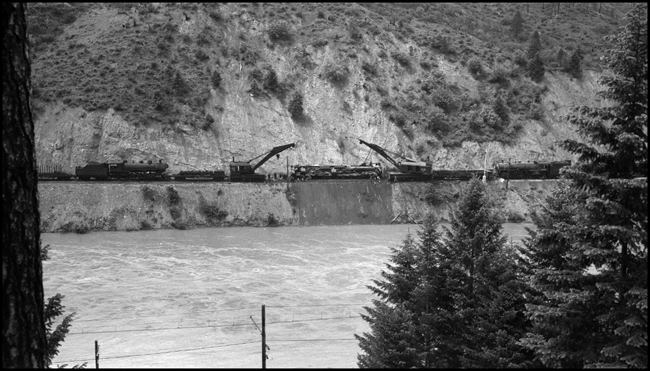 Closer view of two wreckers on work train raising NP 5140 which turned over due to derailment of X5140W when it encountered a broken 130 lb. rail near St Regis, MT.  Wrecking cranes 44 and 45.  Photo taken from north hill, with Milwaukee catinary lines visible over Milwaukee tracks.