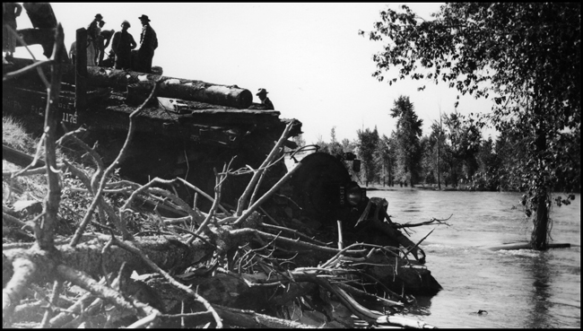View of NP 1356, Class S-4, in water, with a log flat on top of locomotive, as X1356E with 28 log cars derailed into the Bitter Root River near bridge 23.2 caused by high water. Killed Engr McFarland, Fmn Mc Gregor and Bkm D'Orazi