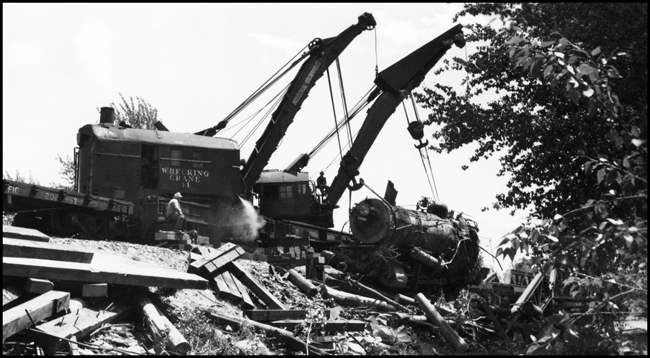 View of the front end of NP 1356, in the slings of Wreckers 41 and 44 as they bring the locomotive out of the Bitter Root River, after the washout derailment on Bridge 23.2. Crew looking on. 