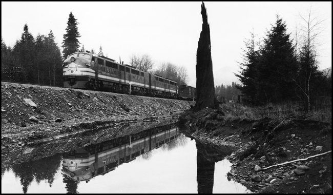 NP X6003E with freight move near Maywood , WA, with nice reflection of train in water.