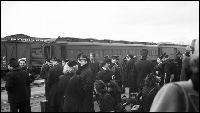 Hollywood actor, Victor Mature, waits for a train at the Yakima WA depot with members of the US Coast Guard.