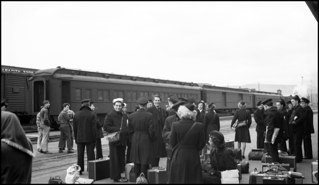 Hollywood actor, Victor Mature, waits for a train at the Yakima WA depot with members of the US Coast Guard.