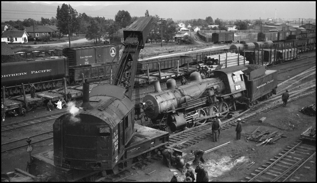 Setting outriggers on wrecker while getting ready to rerail NP 28, Class Y-1, Consolidation locomotive, which has derailed with right side wheels in the dirt in Missoula Yard. 