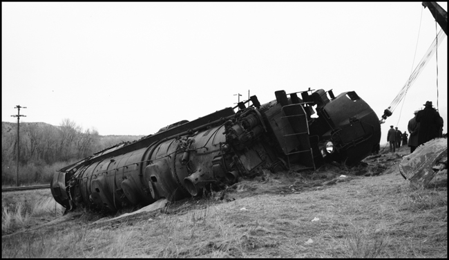 Second No. 3, an equipment special (deadheading Pullmans), derailed at 80 miles per hour on a 40 mile-per-hour curve, about a mile and a half east of Logan, Montana, on November 22, 1945, three days before this photo was taken. A new 250-ton wrecker has just begun the arduous task of dragging the nearly 500-ton Class Z-8 4-6-6-4, no. 5132, back toward the track.