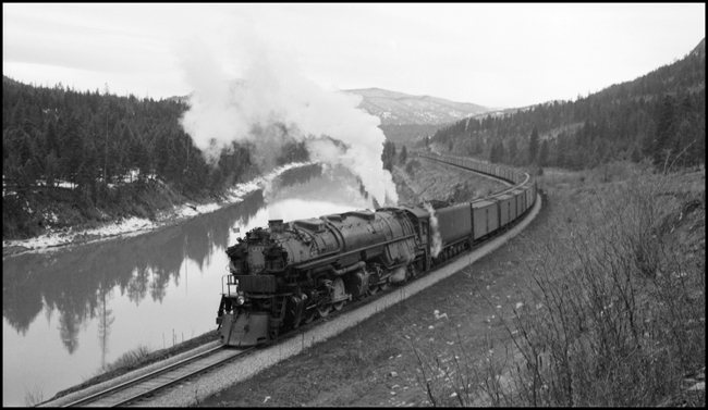 NP Extra 5141 West stopped east of Donlan, Montana, for this publicity photo, for which the weather did not cooperate. The engine is a Class Z-8 4-6-6-4 built by Alco in March 1943. The crew: Engineer Otto C. Behner; Fireman M. H. Slenes; Conductor Byron W. Jenison; and Brakemen T. L. Sparks and L. N. Olsen. Engineer Behner is the oldest among these men, having been hired as a fireman in June 1908 and promoted to engineer in October 1917. The youngest is Olsen, hired as a brakeman in February 1937. The Clark Fork and surrounding mountains make for a very scenic setting. Ron Nixon rode in the cab with the engine crew to Paradise so as to obtain publicity photos of a string of new refrigerator cars that were in the train. Ron had permission to stop the train anywhere he wished for this purpose. The series of photos of this train between Missoula and Paradise were the results of his effort. 