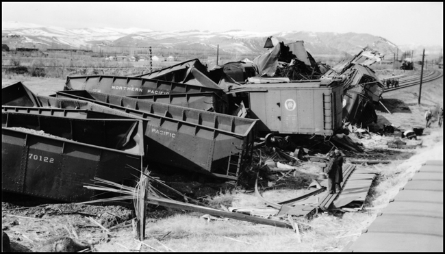 Damage to cars after Extra 5121 West rear-ended the main line local, Extra 1816 West, at Drummond, MT. This accident resulted indirectly from the events surrounding the derailment of wrecker 47 east of Missoula (see RVN09581-09595). Missoula engineer Charles F. Reinke and his fireman had been on a layover in Helena when they were called to take Helena wrecker no. 37 to Missoula to help re-rail wrecker 47. In the meantime, officials decided to use a small wrecker from the Missoula car shop to assist wrecker 27 for that job, so Reinke and his fireman were stopped at Garrison and sent back to Helena. Then, after returning to Helena, they were called short of their legal rest period to handle Extra 5121 West. According to railroad officials, as Reinke approached Drummond he and his fireman had probably fallen asleep and missed block signals protecting the rear of Extra 1816 West. Extra 1816 West's conductor looked out the back of his caboose just in time to see the high speed approach of Extra 5121 West, so he ran into the nearby field. His brakemen were already on the ground giving signals for switching moves they were making at Drummond. The big Z-7 4-6-6-4 type locomotive plowed into the local's wooden caboose at high speed. There were only minor injuries to the crews involved. Conductor Emil Berglin was in charge of Extra 5121 West. Engineer Elmer Walkup and Conductor Malcom McCauley were handling the local.