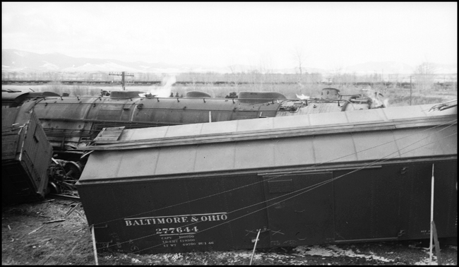 Extra 5121 West rear-ended the main line local, Extra 1816 West, at Drummon, MT. This accident resulted indirectly from the events surrounding the derailment of wrecker 47 east of Missoula (see RVN09581-09595). Missoula engineer Charles F. Reinke and his fireman had been on a layover in Helena when they were called to take Helena wrecker no. 37 to Missoula to help re-rail wrecker 47. In the meantime, officials decided to use a small wrecker from the Missoula car shop to assist wrecker 27 for that job, so Reinke and his fireman were stopped at Garrison and sent back to Helena. Then, after returning to Helena, they were called short of their legal rest period to handle Extra 5121 West. According to railroad officials, as Reinke approached Drummond he and his fireman had probably fallen asleep and missed block signals protecting the rear of Extra 1816 West. Extra 1816 West's conductor looked out the back of his caboose just in time to see the high speed approach of Extra 5121 West, so he ran into the nearby field. His brakemen were already on the ground giving signals for switching moves they were making at Drummond. The big Z-7 4-6-6-4 type locomotive plowed into the local's wooden caboose at high speed. There were only minor injuries to the crews involved. Conductor Emil Berglin was in charge of Extra 5121 West. Engineer Elmer Walkup and Conductor Malcom McCauley were handling the local.